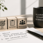 Arbeitsplatz mit Notizbuch, Symbolen für Ziele und Entscheidungen sowie einer Tasse mit der Aufschrift „Klarheit schafft Bewegung“